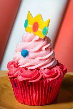 a cupcake with pink frosting and a crown on top is sitting on a plate