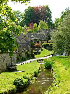 a small river running through a lush green field next to houses on the side of a road