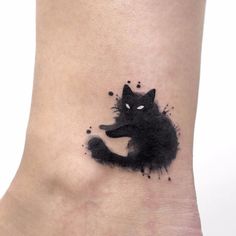 a black cat tattoo on the ankle with watercolor paint splatters all over it