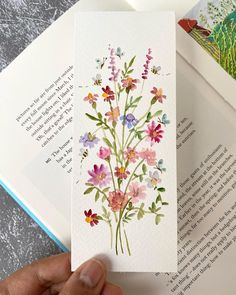 a hand holding an open book with watercolor flowers on it