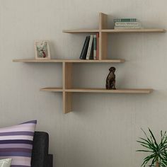 three wooden shelves with books on them against a white wall next to a chair and potted plant