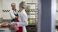 two people in a kitchen preparing food and smiling at each other's company employees