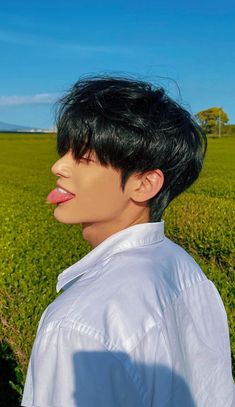 a man with black hair standing in front of a green grass covered field and blue sky