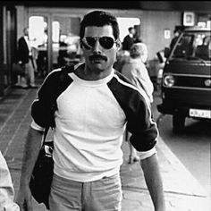 a man with sunglasses and a moustache walking down the street