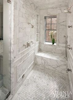 a white bathroom with marble floors and walls, along with a large window in the corner