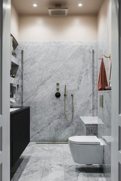 a white toilet sitting in a bathroom next to a walk in shower with marble walls