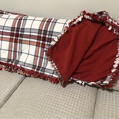 a red and white plaid blanket laying on top of a couch next to a pillow