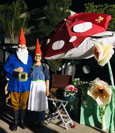 two people dressed up as gnomes standing in front of a tent with flowers on it