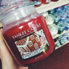 a person holding a jar of yankee candle in front of shelves with candy canes