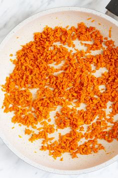 chopped carrots in a white bowl on a marble counter top next to a knife