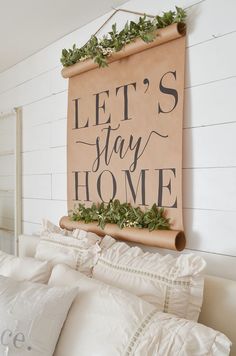 a sign that says let's stay home hanging on the wall above a bed