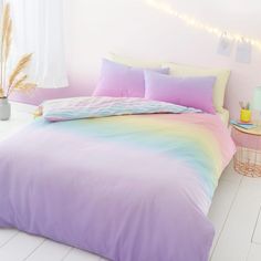 a bed with pastel colored sheets and pillows in a white room next to a window