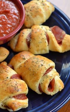 several pigs in a blanket on a blue plate with a small bowl of tomato sauce