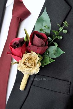 a boutonniere with red roses and greenery on it is worn by a man in a suit