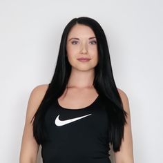 a woman with long black hair and a nike tank top standing in front of a white wall