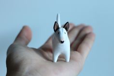 a hand holding a small white dog figurine in it's right hand