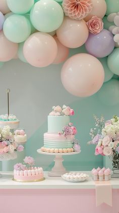 a table topped with lots of cake next to pink and blue balloons hanging from the ceiling