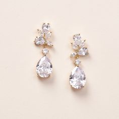 two pairs of diamond earrings on a white surface with one earring dangling from the side