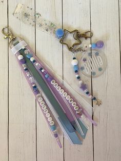 three key chains with beads and charms attached to them on a white wooden surface next to a pair of scissors