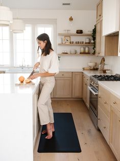 a woman is standing on a mat in the middle of a kitchen while preparing food