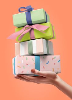 a hand holding three wrapped presents in front of an orange background with sprinkles