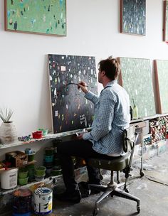 a man sitting at a desk painting on canvases