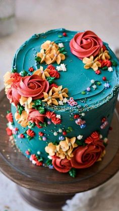 a blue cake with red and yellow flowers on it sitting on a wooden table top