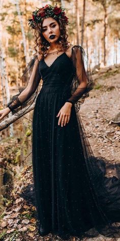 a woman wearing a black dress and flower crown standing in the woods with her hands on her hips