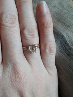 a woman's hand with a diamond ring on top of her left hand, next to a piece of wood