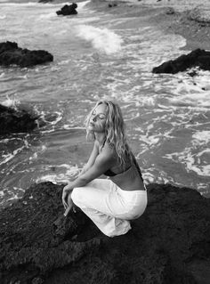 a woman sitting on top of a rock next to the ocean