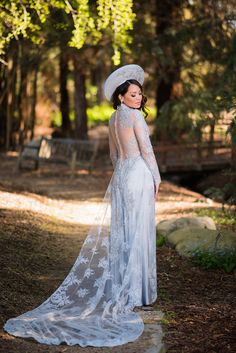 a woman in a white dress and hat is posing for a photo with trees behind her