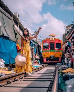 a woman in a yellow dress is waving at the camera while standing on train tracks