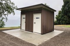 two brown and white portable toilets sitting on top of a dirt field next to the ocean