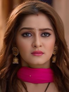 a woman with long brown hair wearing earrings and a pink dress is looking at the camera