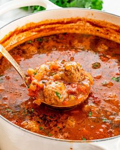 a ladle full of meatball soup is being held up by a wooden spoon