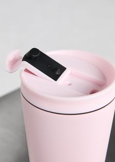 a pink coffee cup with a black lid and spoon sticking out of it's side