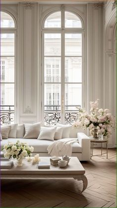 a living room filled with white furniture and flowers in vases on the coffee table