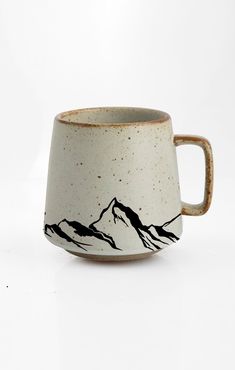 a white and black coffee cup with mountains on the side, sitting in front of a white background