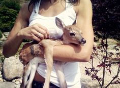 a woman holding a baby deer in her arms