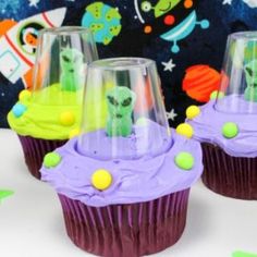 three alien cupcakes with purple frosting and green sprinkles on them