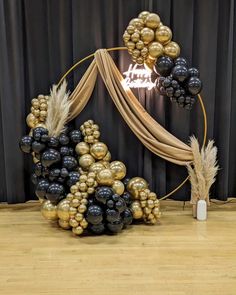 a balloon arch with black and gold balloons in the shape of a pyramid on a wooden floor