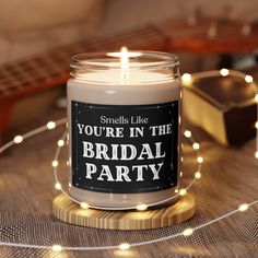 a candle is sitting on a table with some string lights around it that says, you're in the bridal party