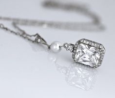 Classically elegant and sophisticated! Emilia cz crystal bridal necklace made in a radiant cut with a frame of tiny cz crystals for a beautiful sparkling accessory that will suit your dress, whatever style. The 18K rhodium setting has delicate carving around the sides so your necklace is pretty from all aspects!A Swarovski pearl in your custom color adds a personalized touch your Emilia necklace.Measures: 2" (5 cm) top to bottom. 0.5" (1.2cm) widest point.All components are  rhodium plated sterl Elegant Rectangular Pendant Necklace For Wedding, Classic Wedding Jewelry With Rectangular Pendant, Elegant Rectangular Pendant Jewelry For Wedding, Wedding Necklace With Square Pendant And Brilliant Cut, Wedding Necklace With Brilliant Cut Square Pendant, Elegant Square Pendant Jewelry For Wedding, Brilliant Cut Square Pendant Necklace For Wedding, White Gold Rectangular Pendant For Wedding, Rectangular White Gold Necklace For Wedding