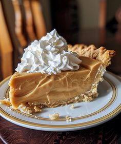 a piece of pie with whipped cream on top sits on a white and gold plate