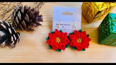 red and green crochet flower earrings next to christmas presents on wooden table with pine cone