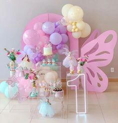 a table topped with lots of balloons and cake next to a giant butterfly balloon wall