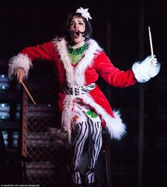 a man dressed in costume holding a stick and singing into a microphone while standing on stage