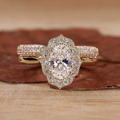 an oval shaped diamond ring on top of a wooden surface with leaves in the background