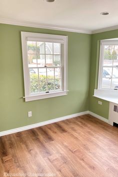 an empty room with green walls and white trim on the windows, wood flooring