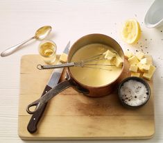 a wooden cutting board topped with a bowl filled with liquid next to sliced lemons